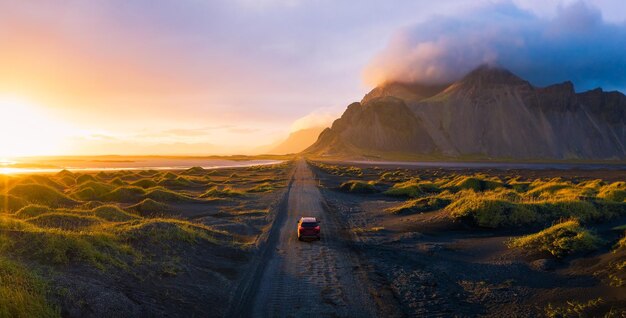 Gravel road at sunset with vestrahorn mountain and a car driving iceland | The Web Univers